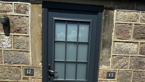 A black door with a grid pattern window, set in a stone wall with numbered plaques '12' and '13'. - Chevin End Guest House (Ilkley)