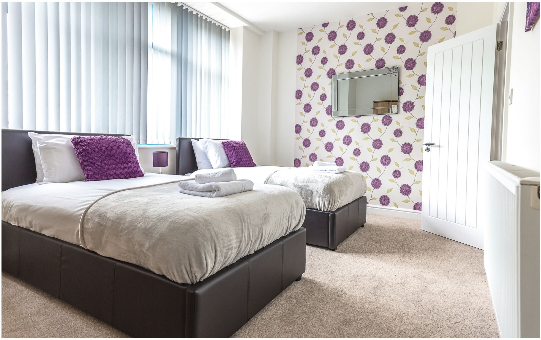 A bedroom with a large bed, two bedside tables, a mirror, and a door.