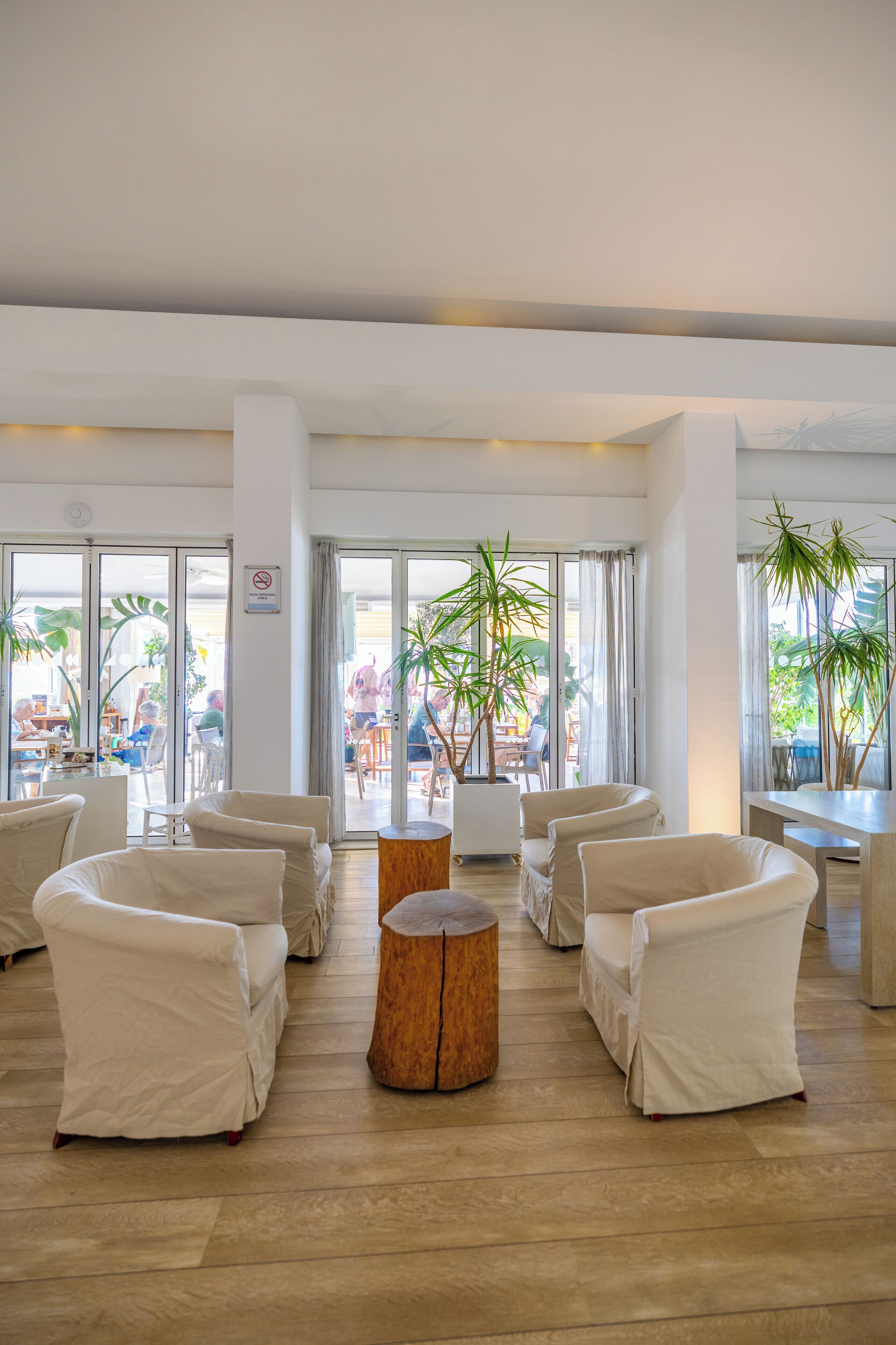 Un espace intérieur spacieux, meublé de blanc, avec une table basse en bois et de grandes fenêtres laissant entrer la lumière naturelle.