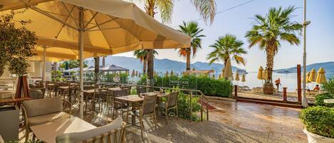 An outdoor seating area with tables and chairs, umbrellas, and potted plants.