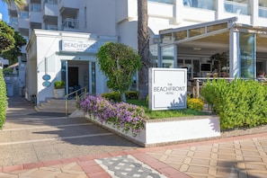 Entrada de hotel con un letrero, escalones y un área ajardinada con plantas.