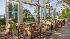 A restaurant with outdoor seating, large windows, and palm trees. - The Beachfront Hotel Adult Only 16 Plus (Marmaris)