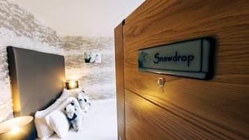 Una habitación de hotel con una cama, una mesita de noche con lámpara y una puerta de madera con la etiqueta 'Snowdrop'.