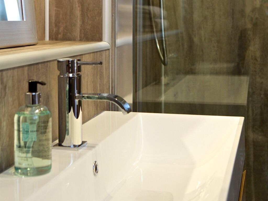 A bathroom with a white sink, a handheld showerhead, and a bottle of liquid soap.