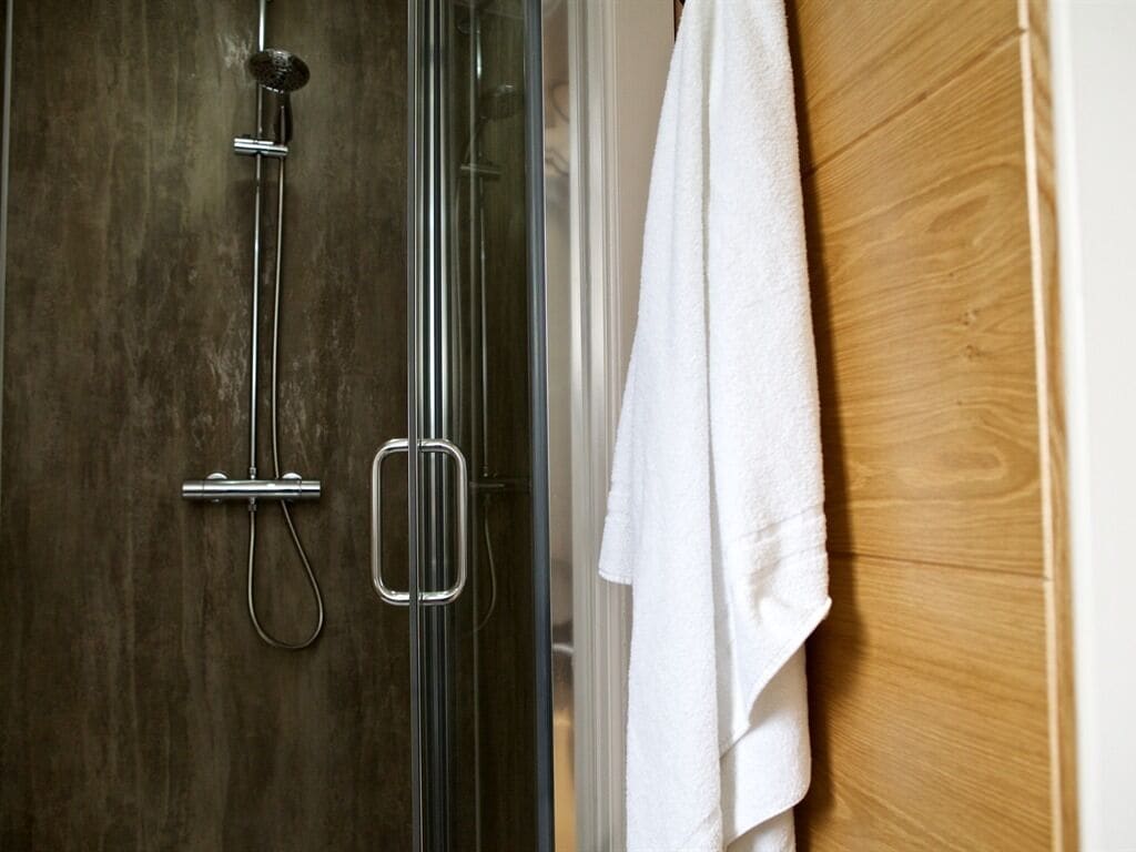 A shower with a glass door, a towel hanging on the wall, and a wooden panel.