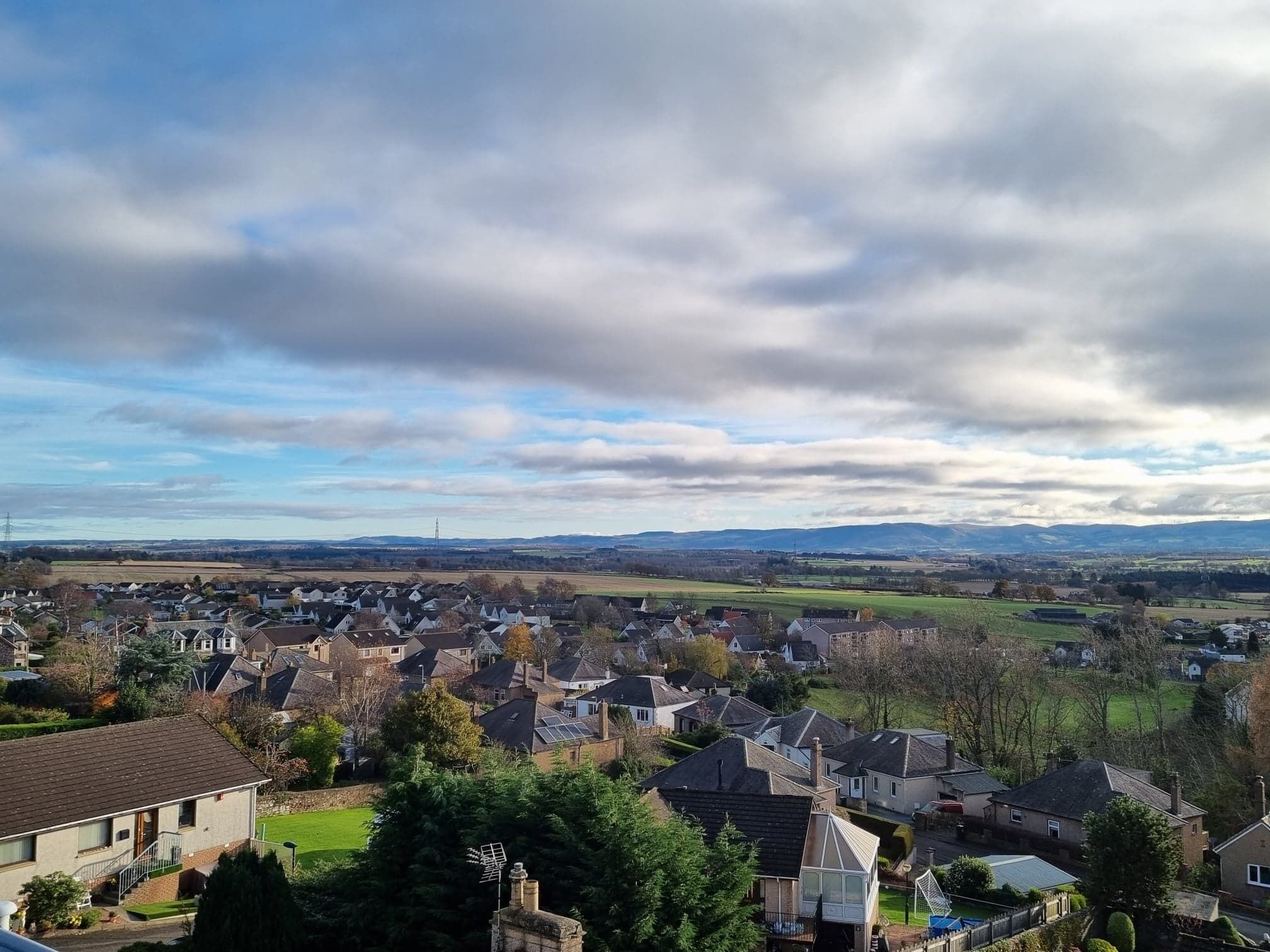 Un quartier résidentiel avec des maisons, un ciel dégagé et des collines à l’horizon.