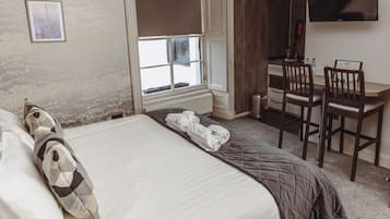 A hotel room with a bed, a desk, two chairs, a TV, and a window.