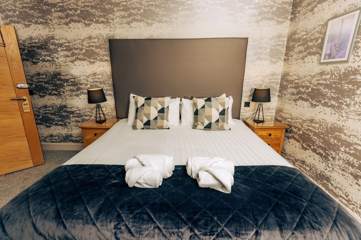 A hotel room with a large bed, two bedside tables with lamps, a wooden door, and a textured wall.