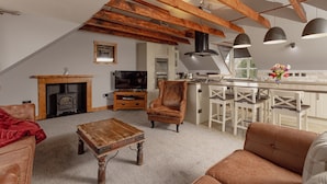 A cozy loft-style living area with exposed wooden beams, a fireplace, a kitchen with bar stools, and a comfortable seating area. - The Tower Gastro Pub & Apartments (Crieff)