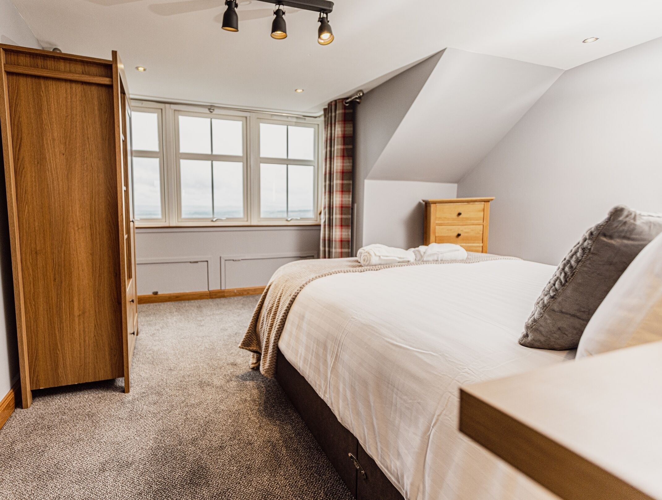 Un dormitorio con una cama grande, un armario de madera, un pequeño tocador de madera y una ventana con cortinas.