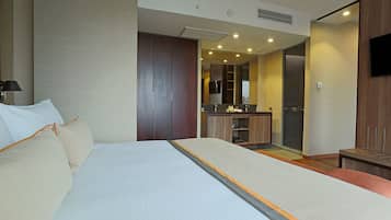 Una habitación de hotel con una cama grande, un escritorio pequeño, un espejo y una zona de kitchenette.