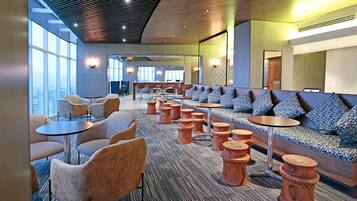 A modern lounge with seating arrangements, including sofas and round tables, and a view of the city through large windows.
