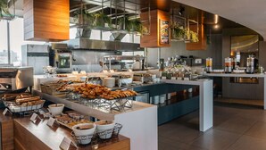 Un desayuno buffet moderno con diversos pasteles, bebidas calientes y una cocina limpia y bien iluminada.