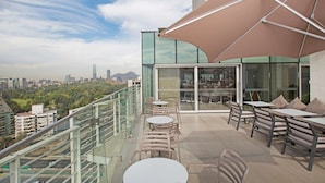 Una terraza en la azotea con mobiliario exterior, un parasol grande y vistas a la ciudad.