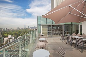Una terraza en la azotea con mobiliario exterior, un parasol grande y vistas a la ciudad.