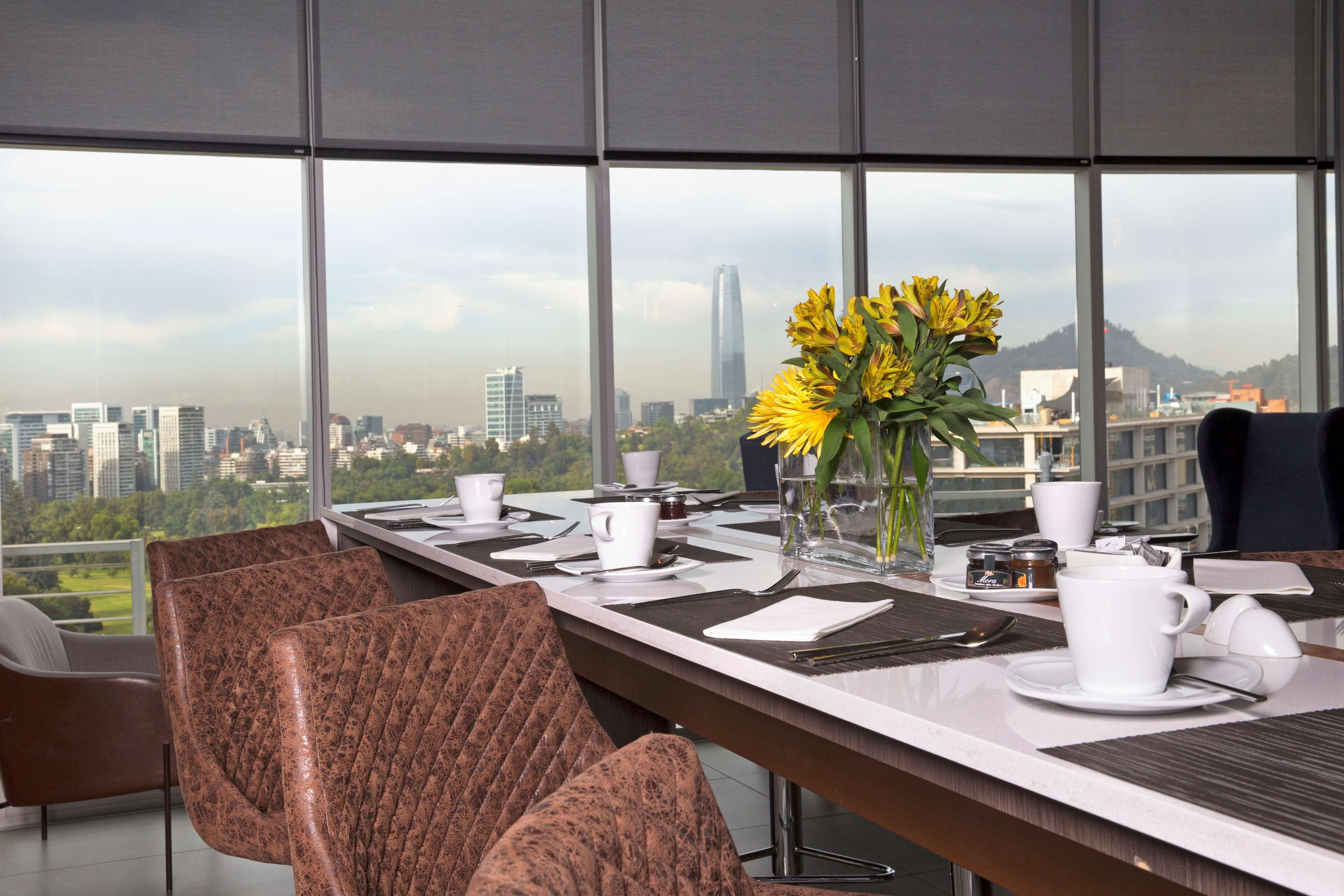 Un comedor moderno con vistas a la ciudad, una mesa larga preparada para una reunión y asientos cómodos.