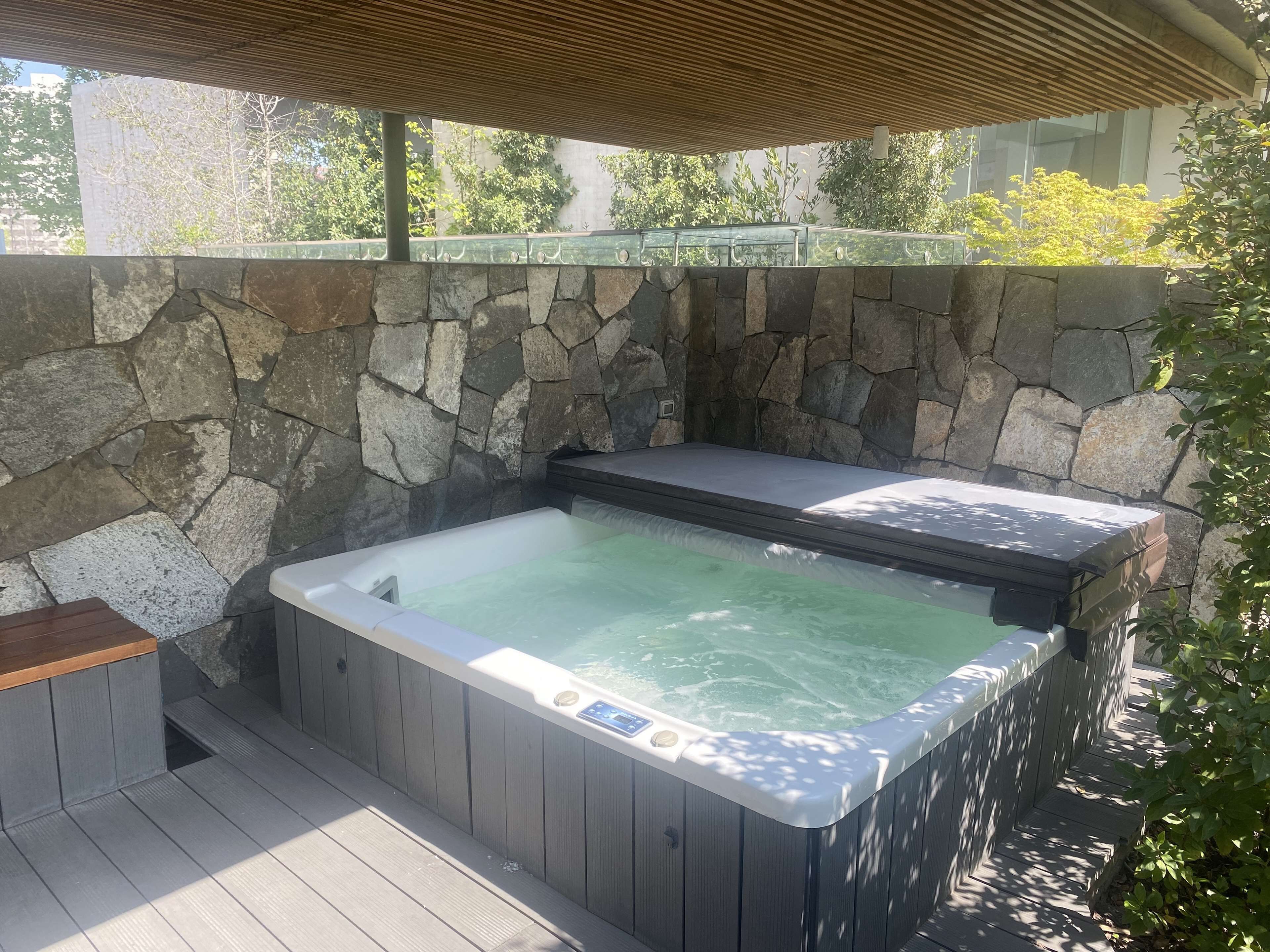 Ein Whirlpool mit Steinwand, Holzterrasse und Glasgeländer.