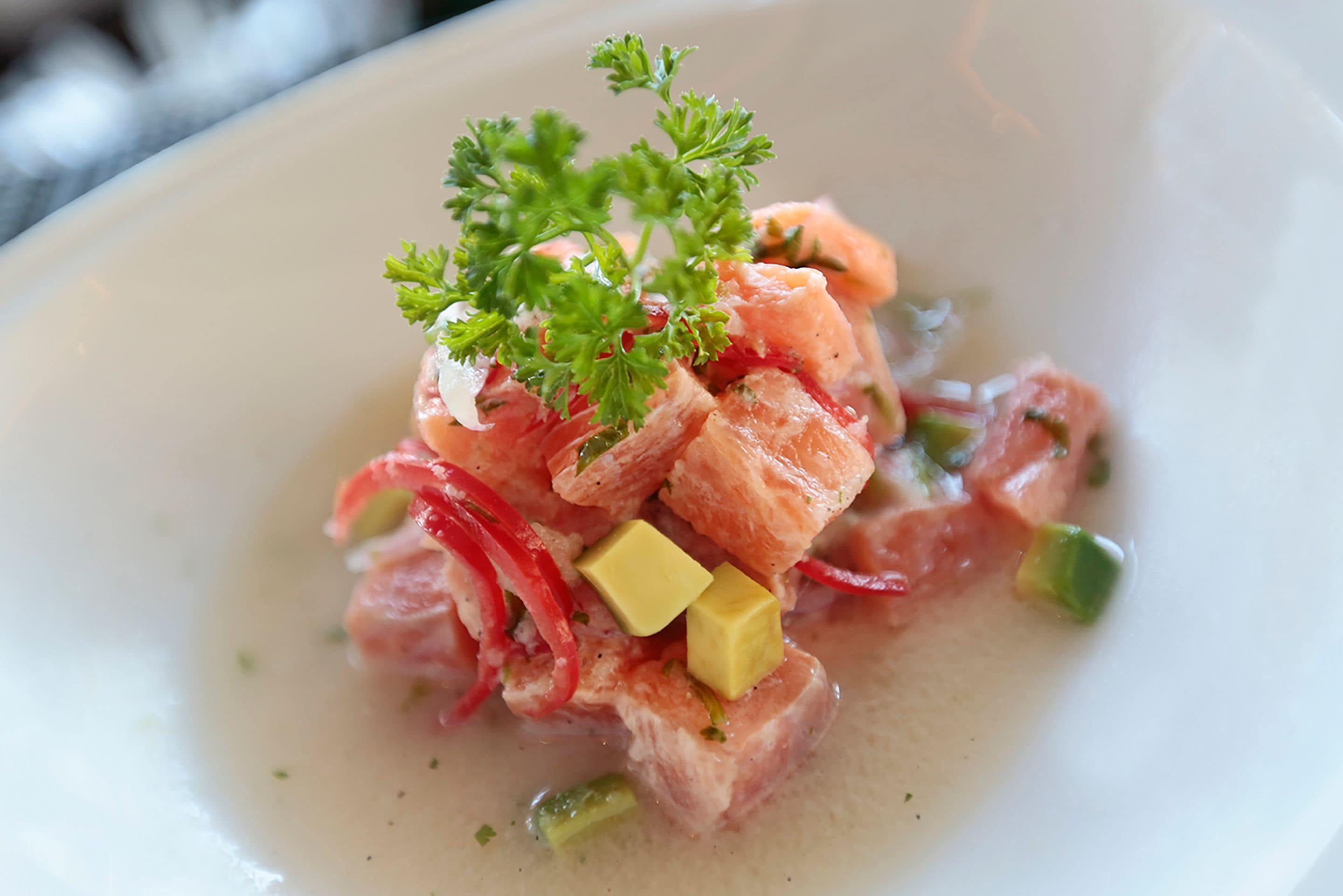 A dish with cubed salmon, red peppers, and green onions, garnished with parsley.