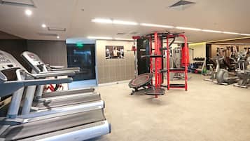 A gym with treadmills, a red cable machine, and a wall-mounted TV.
