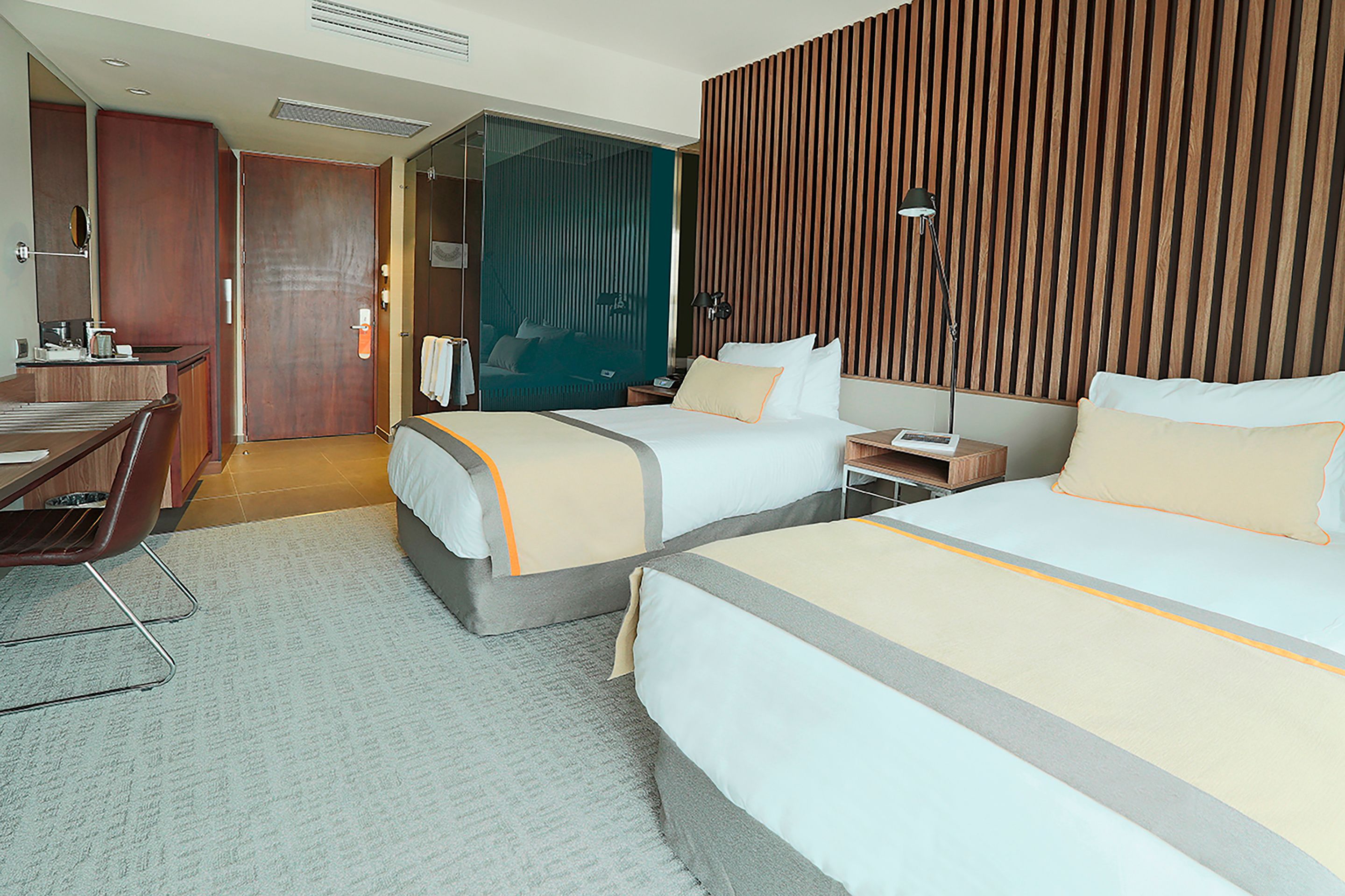 A hotel room with two beds, a desk, a chair, and a wardrobe.