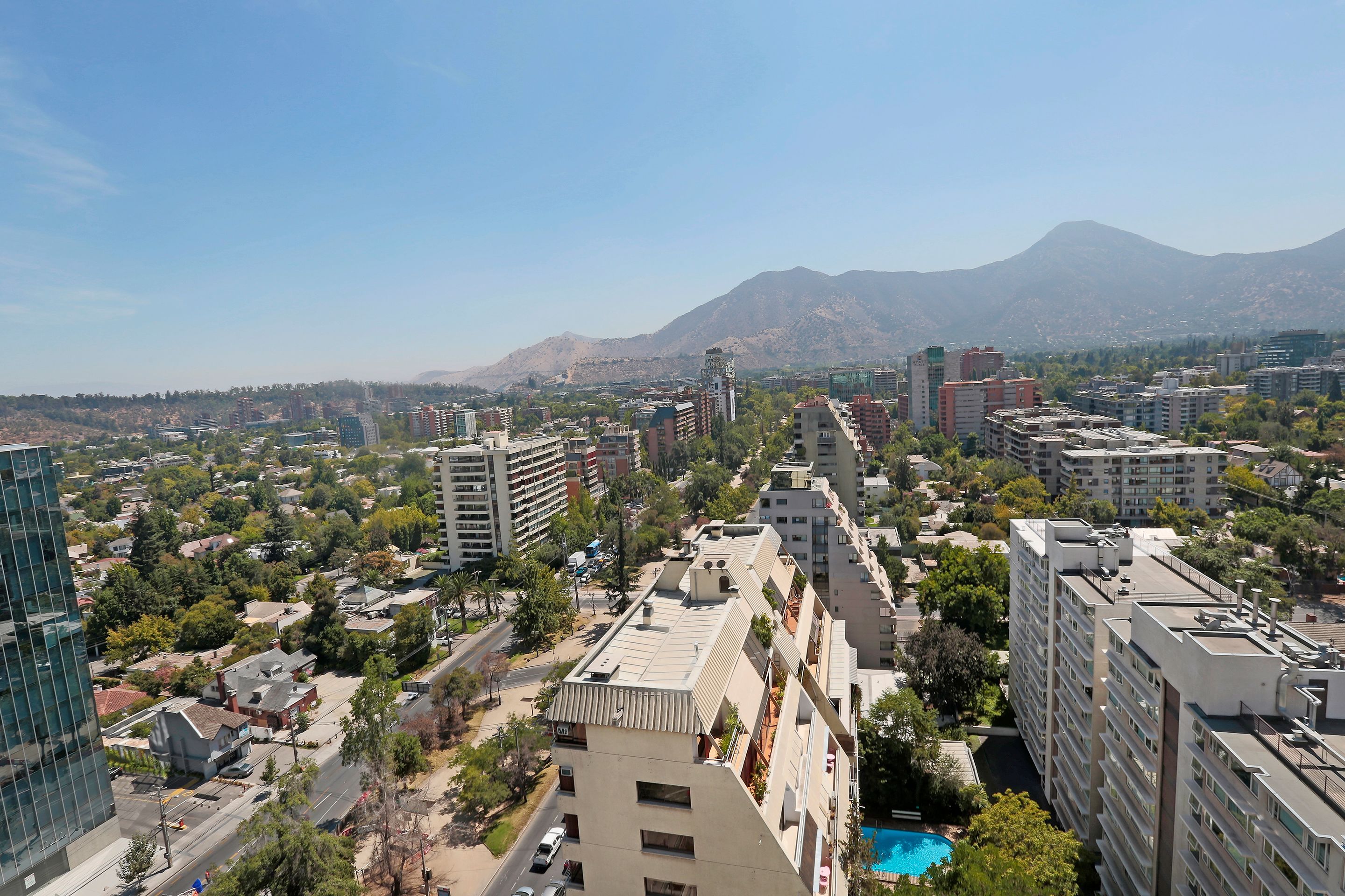 A cityscape with modern buildings, a clear sky, and mountains in the background.