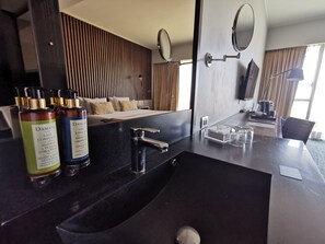 Ett modernt badrum med en svart tvättställ, två flaskor lotion, en spegel och en säng i bakgrunden.