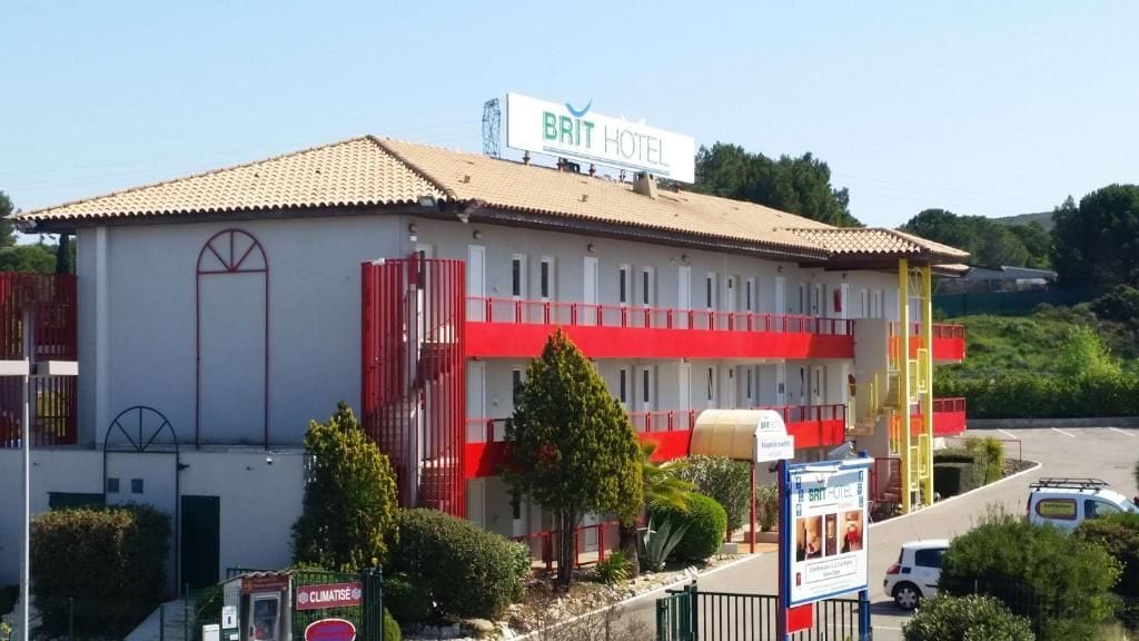 A BRIT HOTEL with a red and white facade, a balcony on the second floor, and a parking area in front.