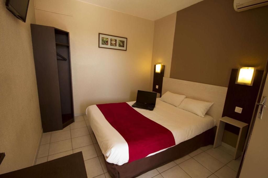 Een hotelkamer met een bed, een bureau, een stoel, een kledingkast en een aan de muur bevestigde televisie.