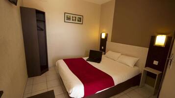 Een hotelkamer met een bed, een bureau, een stoel, een kledingkast en een aan de muur bevestigde televisie.