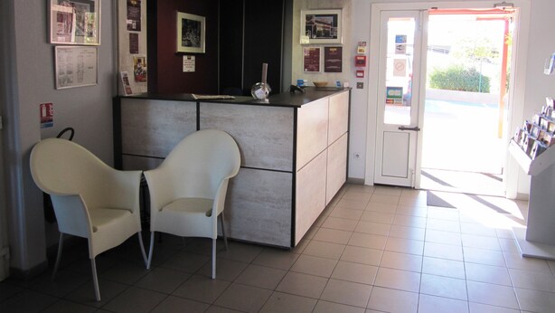 A reception area with a counter, two white chairs, and a door leading outside. - Brit Hotel Essentiel Sète Balaruc (Balaruc-le-Vieux)