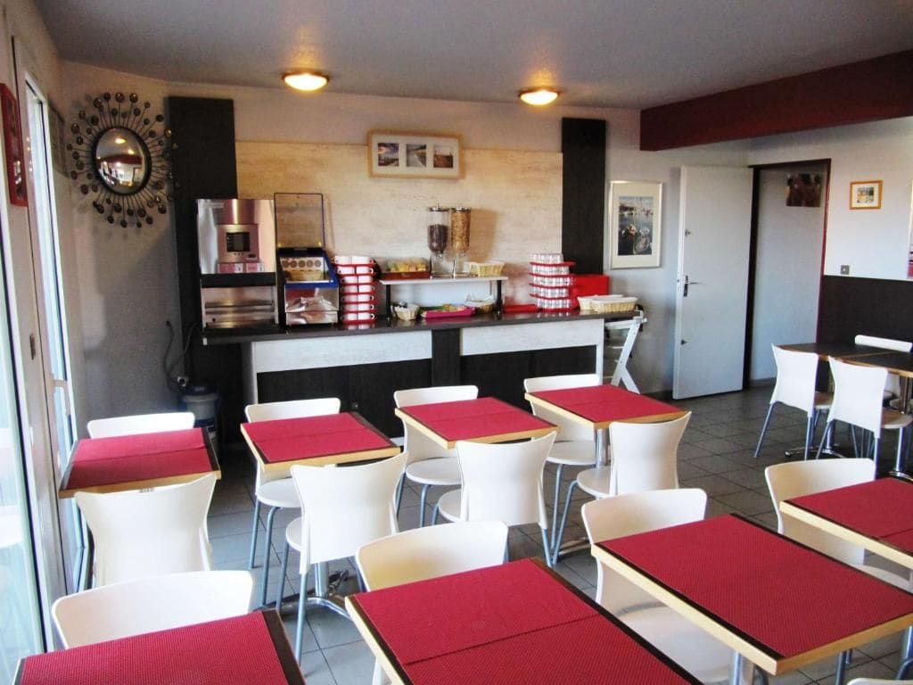 Un espace repas avec des tables et des chaises, un coin cuisine équipé d’appareils électroménagers et un miroir fixé au mur.