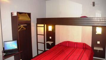 Una cama individual con colcha roja, un ordenador portátil sobre un escritorio y un armario con perchero.