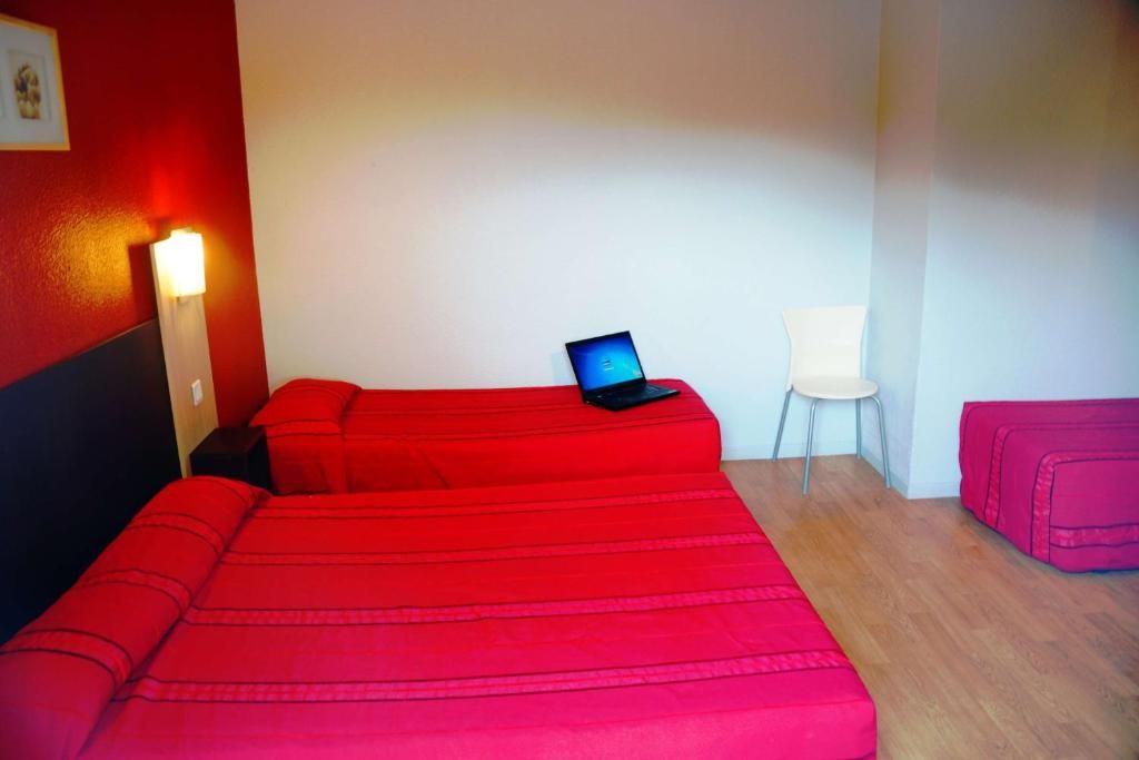 A room with two beds, a laptop on one bed, a chair, and a suitcase.