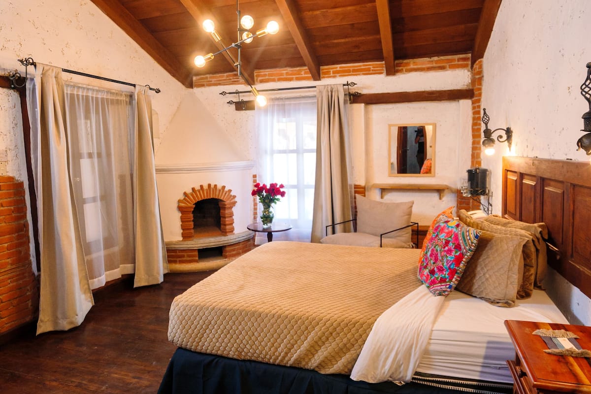 Ein gemütliches Schlafzimmer mit Holzbalkendecke, einem Bett mit Decke, einem Nachttisch und einer Kommode.