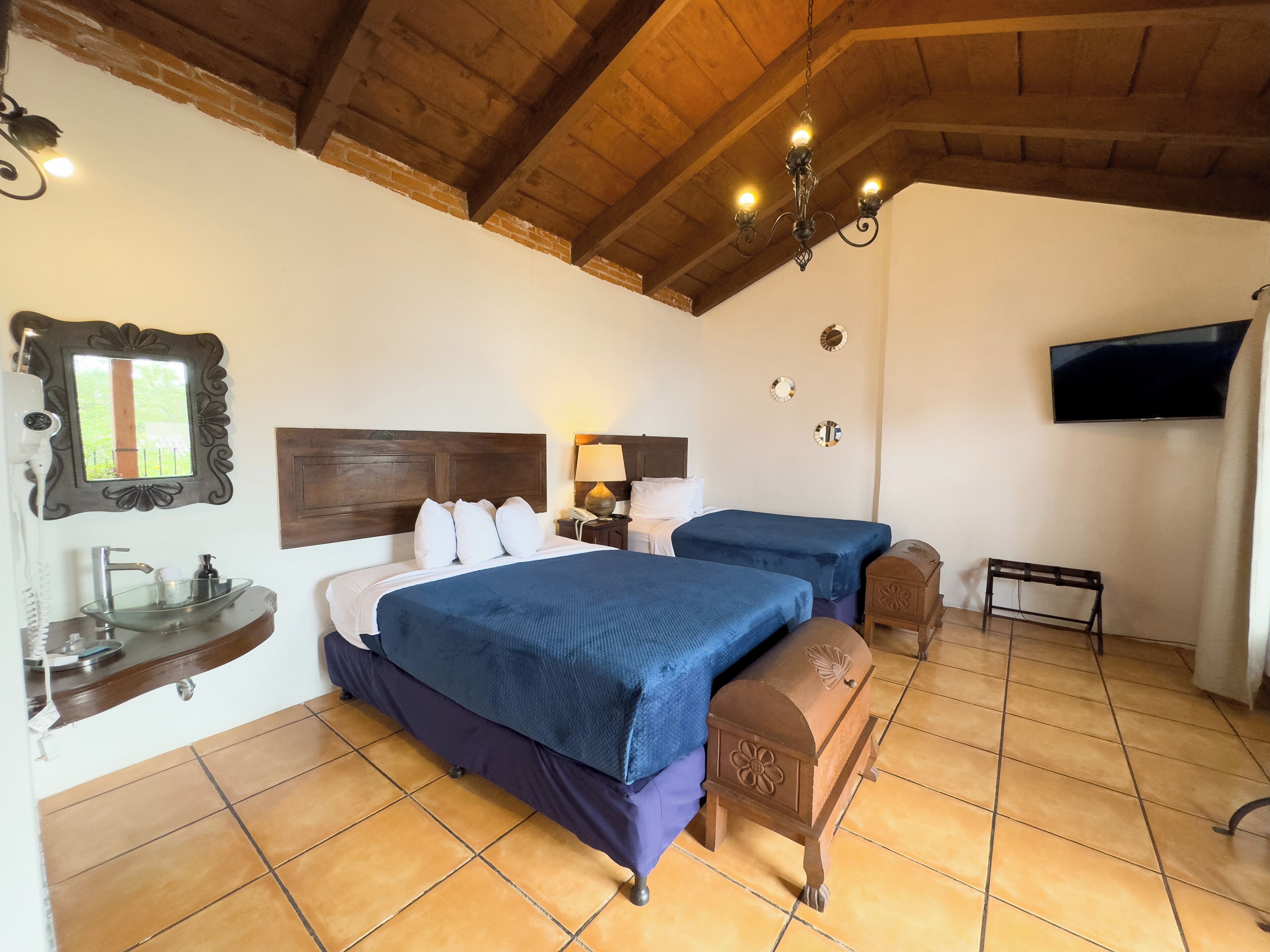A bedroom with two beds, a wooden ceiling, a TV, and a small wooden bench.