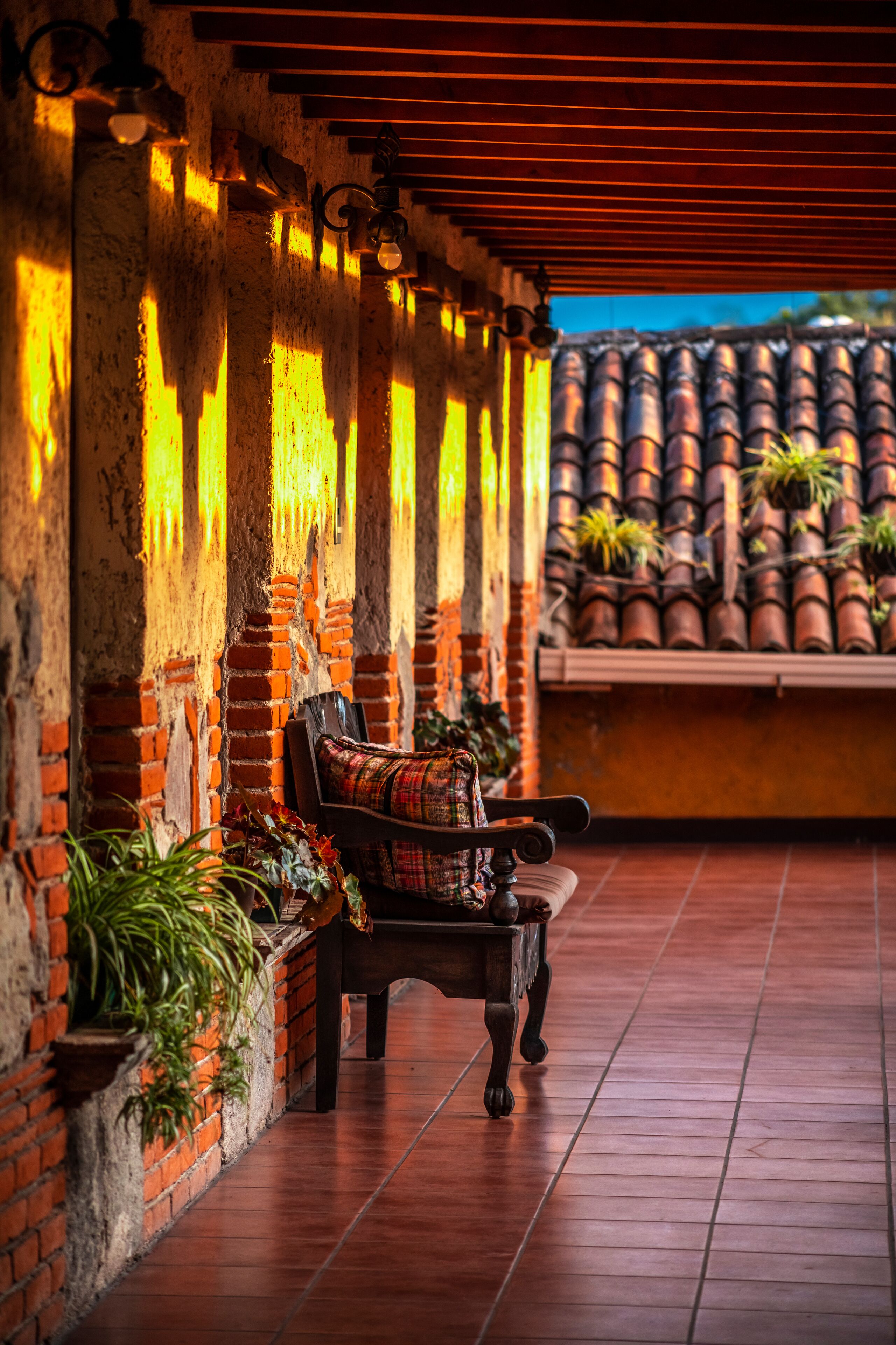 A bench with a patterned cushion in a covered outdoor area with brick walls and terracotta tiles.