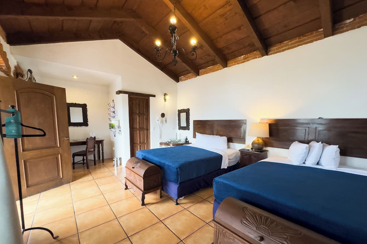Ein Zimmer mit zwei Betten, einer Holzbalkendecke, einem Schreibtisch mit Stuhl und einer Tür.