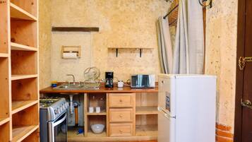 Une cuisine compacte équipée d’une cuisinière, d’un four, d’un four à micro-ondes et d’un réfrigérateur. On y trouve des étagères en bois et un évier.