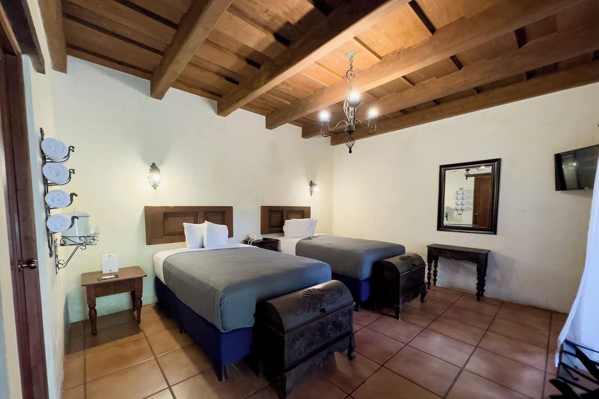 Ein Schlafzimmer mit zwei Betten, einer Holzbalkendecke, einem kleinen Tisch und einem Spiegel.