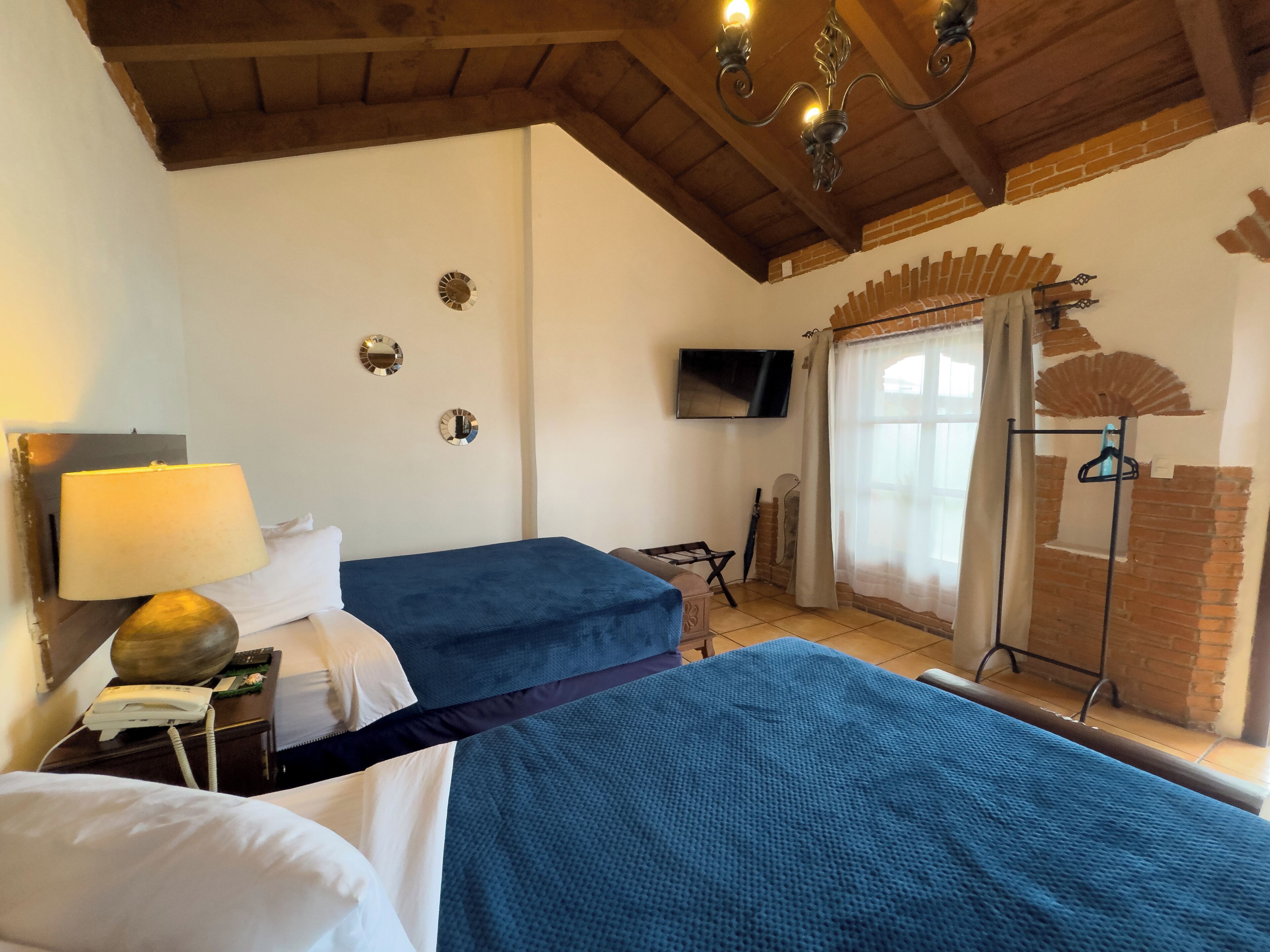 A room with two beds, a TV, a lamp, and a brick wall.