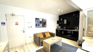 A modern living room with a sofa, coffee table, and a kitchen area with cabinets and appliances. - Room Home Stay (London)