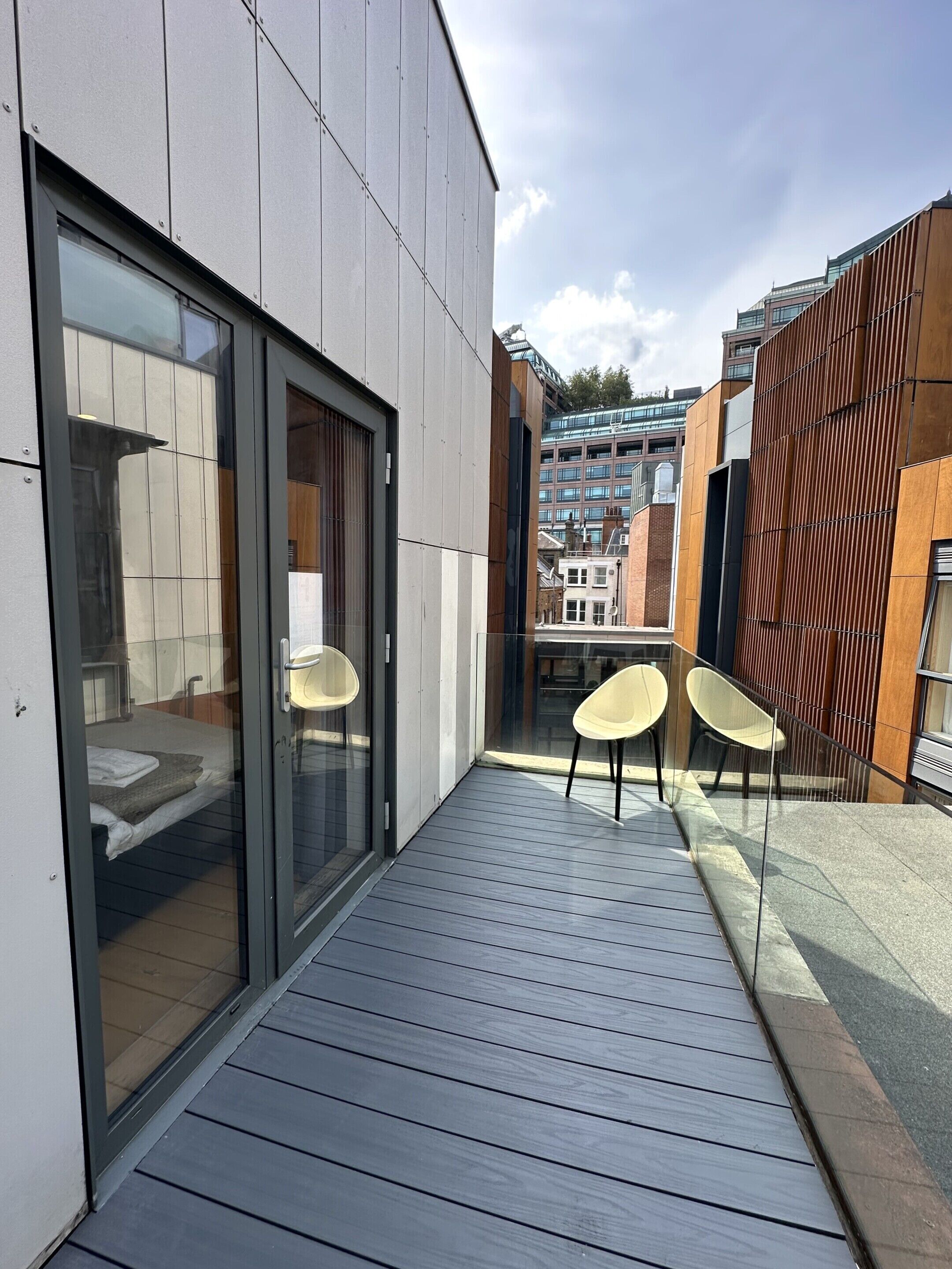 A modern building with a balcony, two chairs, and a glass door leading to a room.