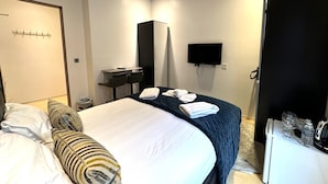 A hotel room with a bed, a desk with two chairs, a television, and a wardrobe. - Room Home Stay (London)