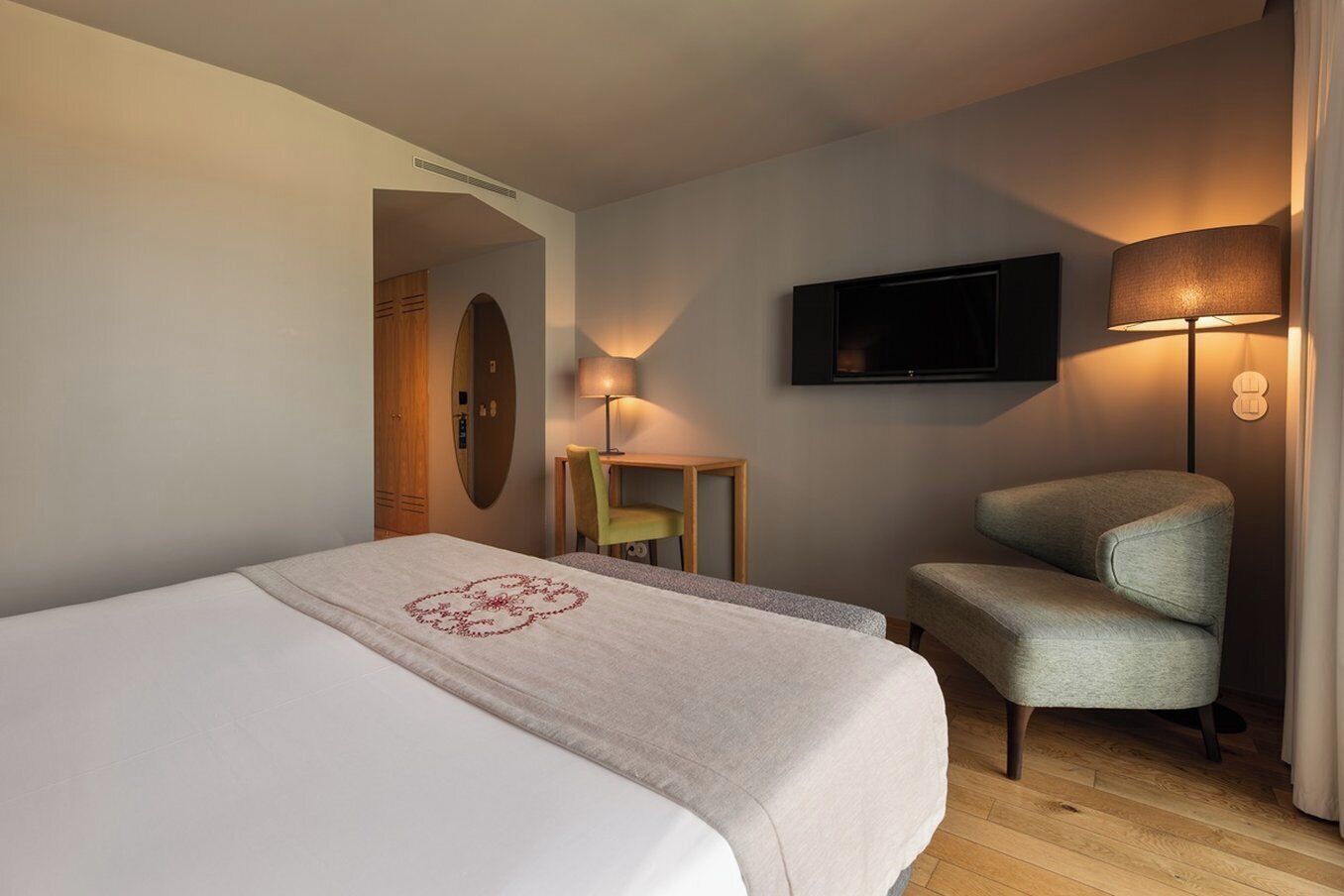 A hotel room with a bed, a TV, a desk, a chair, and a lamp.