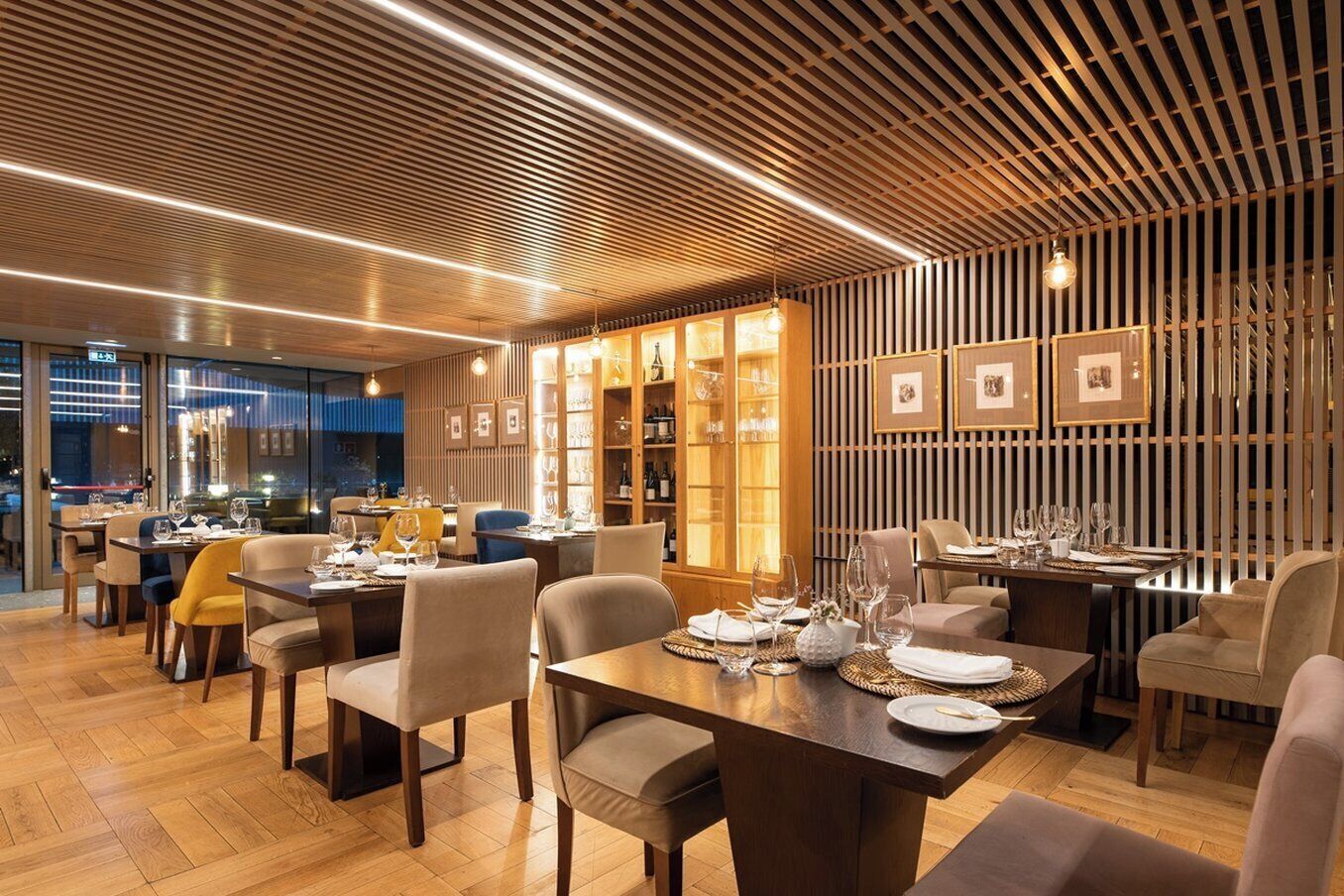 A restaurant with wooden paneling, tables set with glasses and plates, and framed pictures on the wall.