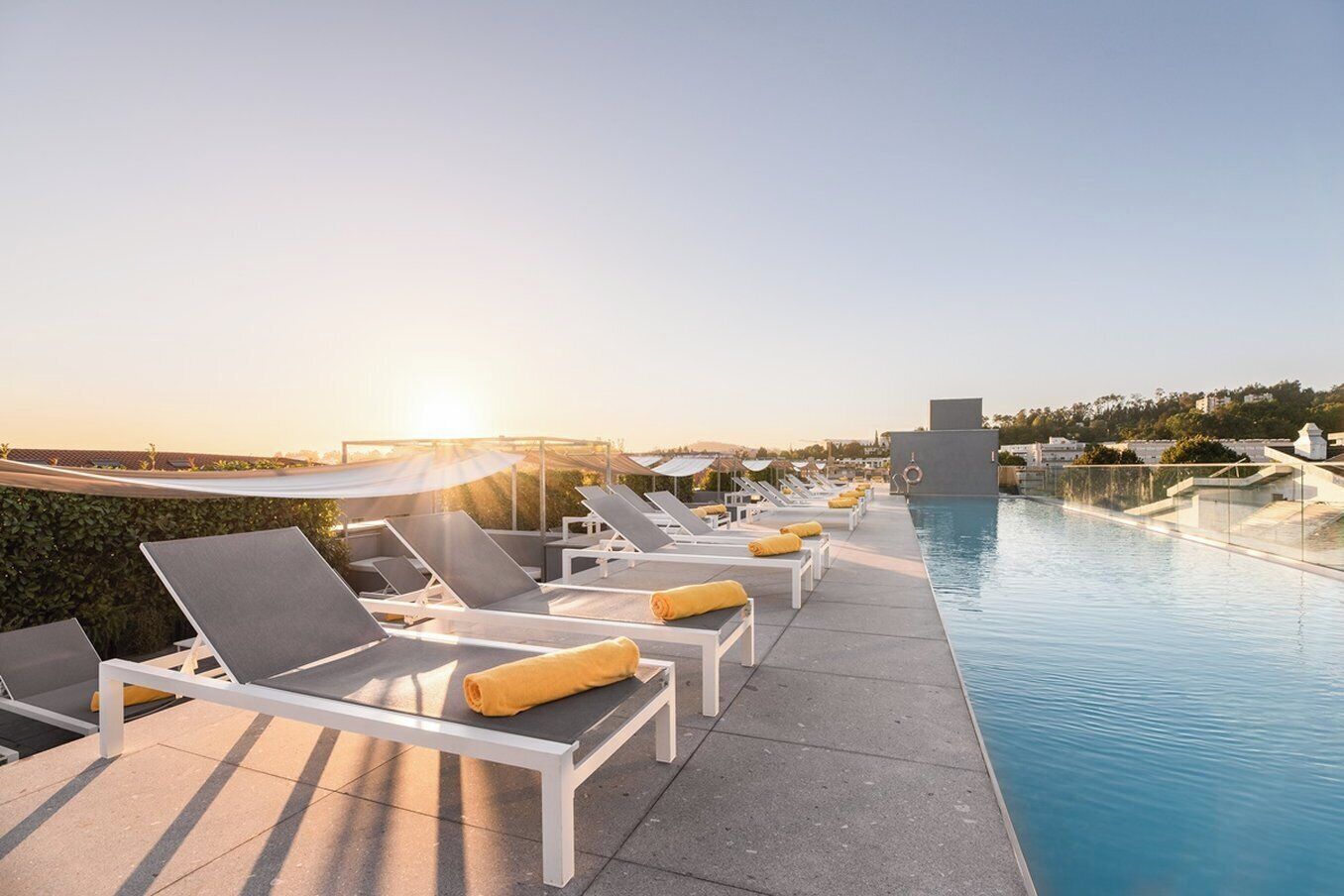 A rooftop pool area with sun loungers and a clear view of the sunset.