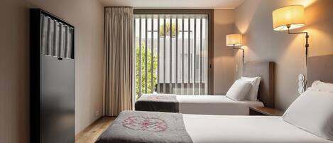 Habitación de hotel con dos camas, un armario, una ventana con cortinas y lámparas fijadas a la pared.