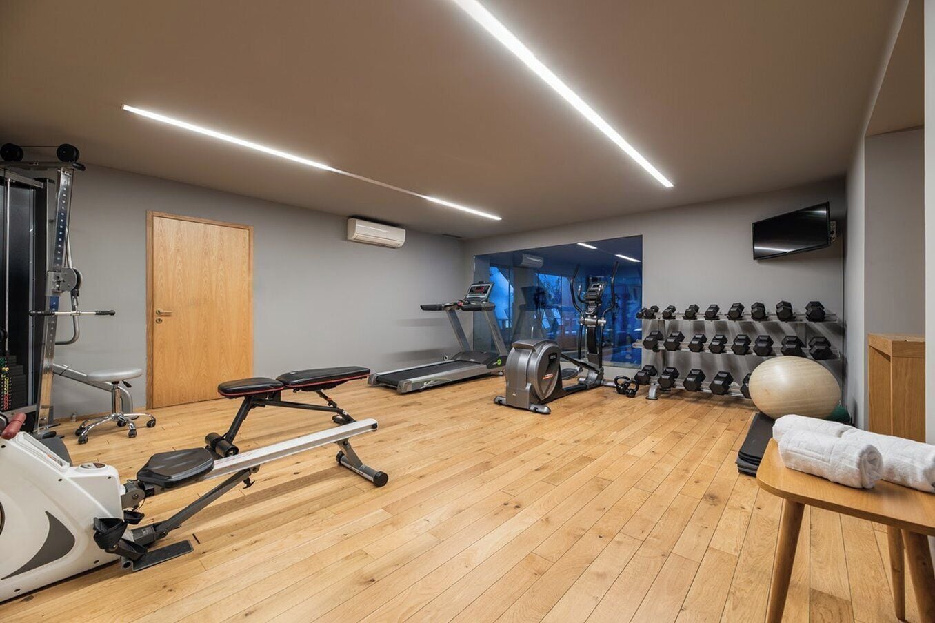 Un gimnasio con máquinas de cardio, estaciones de pesas y un espejo grande.