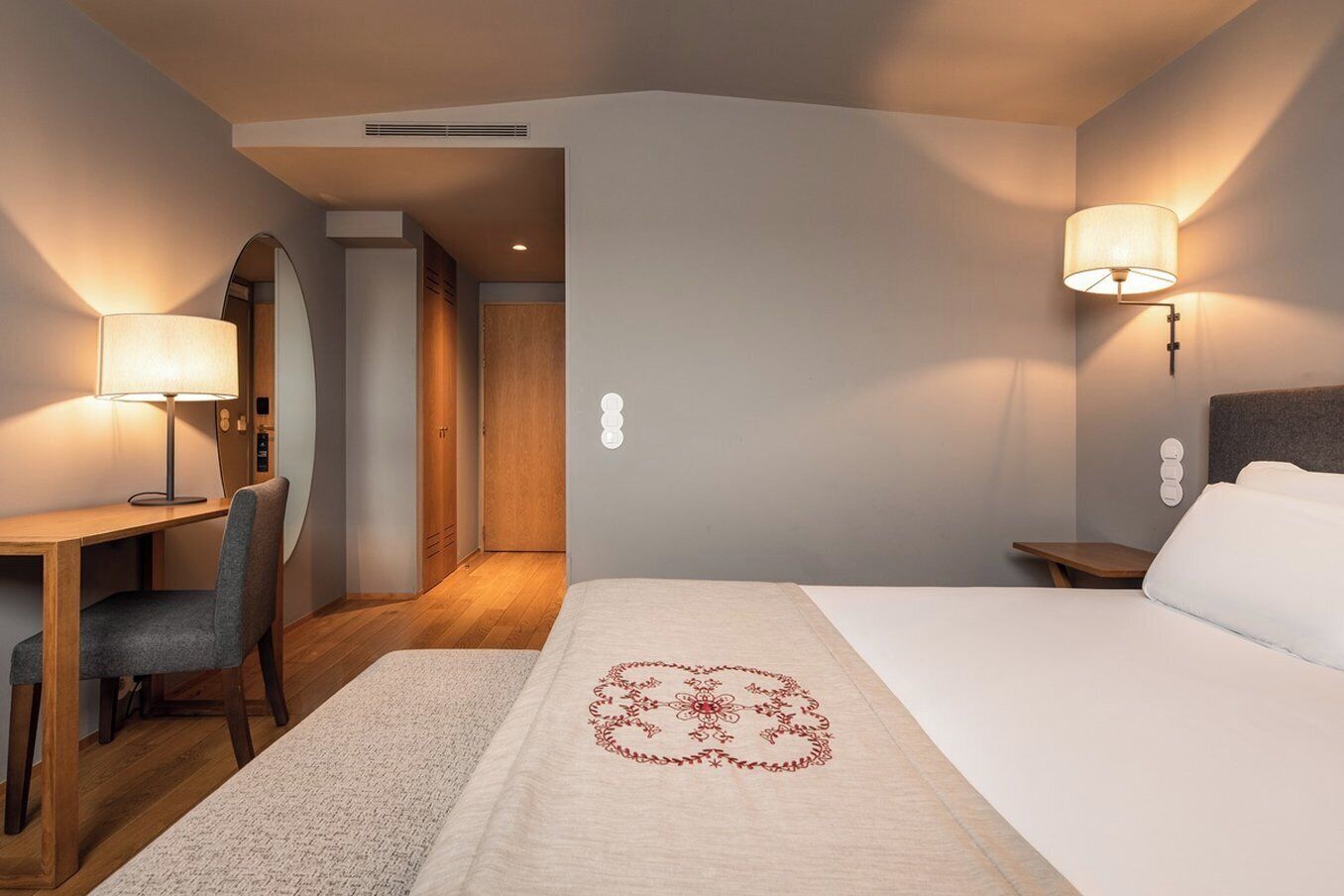 A hotel room with a bed, desk, chair, and bedside table.