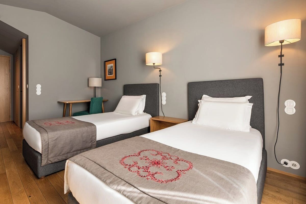 Een hotelkamer met twee bedden, een tafeltje, een stoel en een wandlamp.